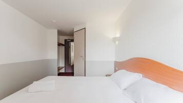 Quarto de hotel com cama bem arrumada, cabeceira de madeira e luminária fixada na parede.