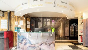 A reception desk with a glass top, surrounded by a mural, and a check-in counter with a digital display. - Logis Hôtel Restaurant Cap Hôtel. (Noyelles-Godault)