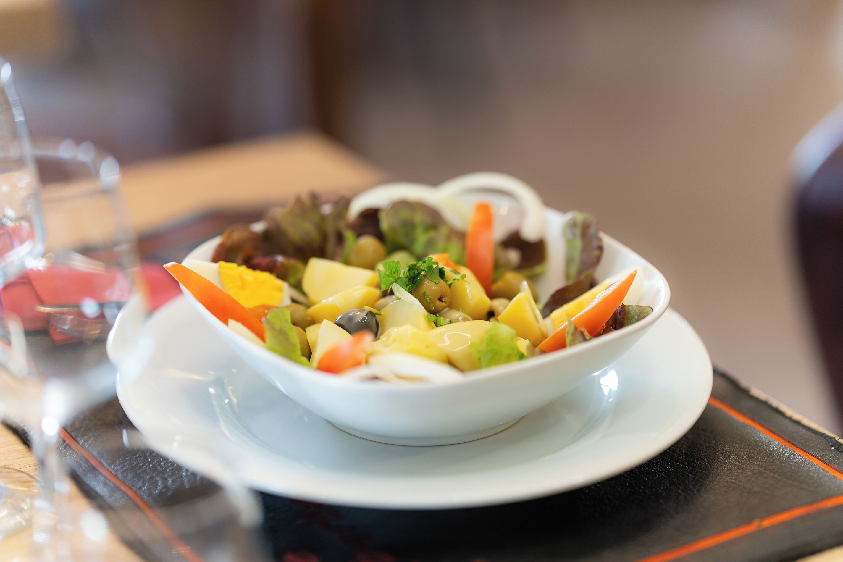 A bowl of mixed vegetables on a white plate with a black placemat underneath.