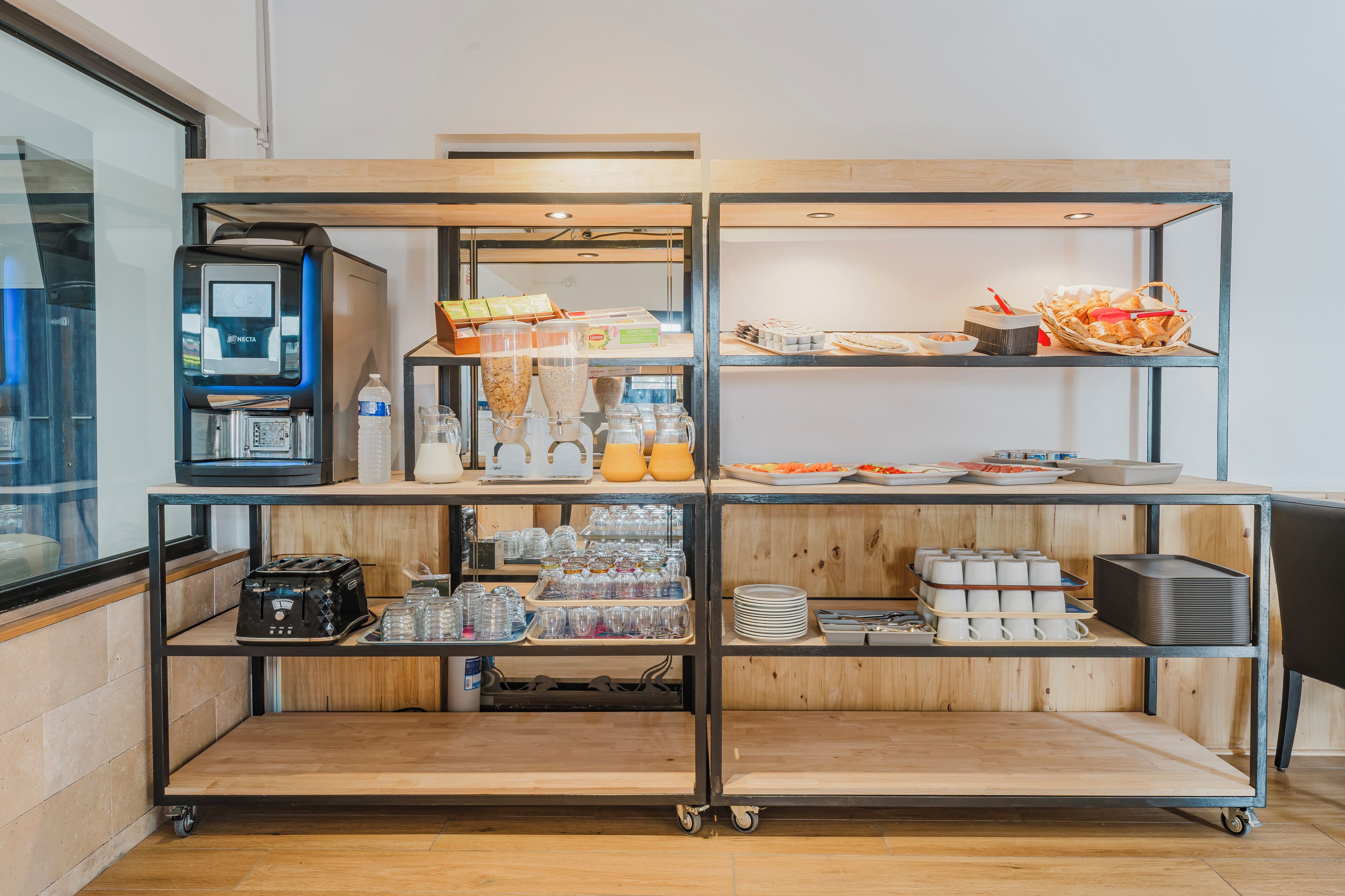 Estação de pequeno-almoço com serviço livre, incluindo máquina de café, diversos alimentos e acompanhamentos.