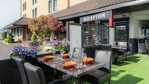 An outdoor dining area with tables set for two, a reception sign, and a building in the background. - Logis Hôtel Restaurant Cap Hôtel. (Noyelles-Godault)