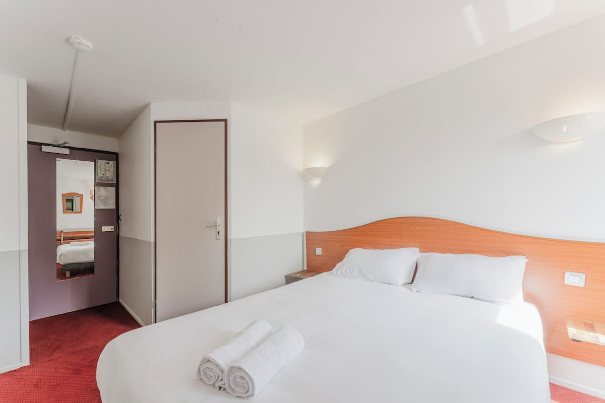 A hotel room with a large bed, a wooden headboard, white bedding, a red carpet, and a door leading to a bathroom.