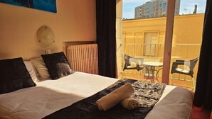 Une chambre d’hôtel avec un lit, une grande fenêtre et un balcon équipé de chaises.