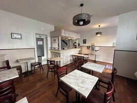 A restaurant interior with marble tables, wooden chairs, a bar area, and a small round table with a menu.