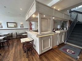 A restaurant with a counter, wooden tables, and chairs.