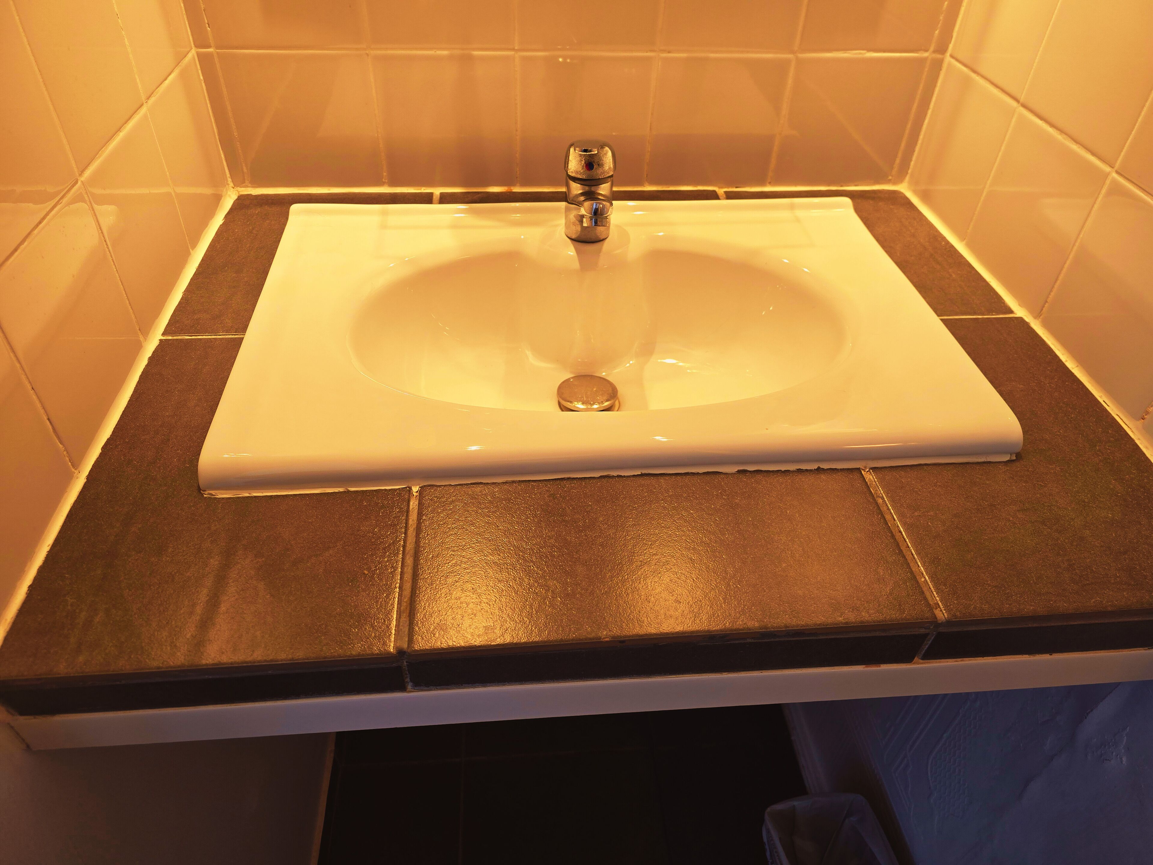 Un baño con lavamanos blanco, encimera oscura y paredes con azulejos.