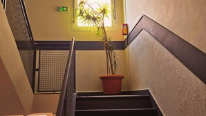 Un escalier avec un pot de plante à sa base, une fenêtre donnant sur un paysage verdoyant et un détecteur d’incendie fixé au mur.