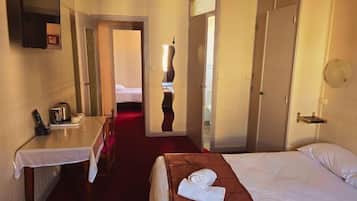 Une chambre d’hôtel avec un lit, un bureau, une chaise et une salle de bain visible à travers une porte ouverte.