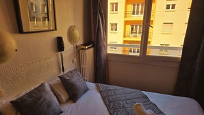 Une chambre d’hôtel équipée d’un lit, d’oreillers, d’un téléphone sur la table de chevet, d’un radiateur et d’une fenêtre donnant sur un immeuble.