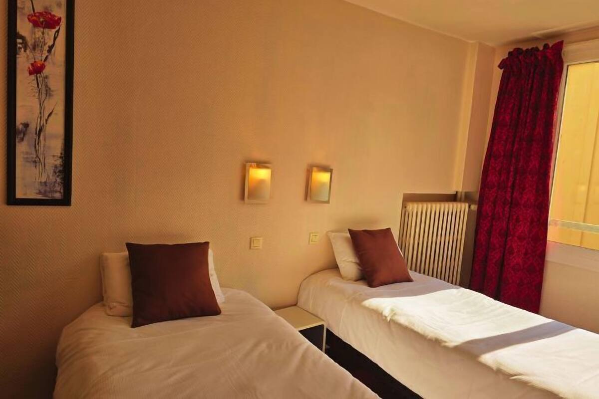 Ein Hotelzimmer mit zwei Einzelbetten, einem Heizkörper, einem roten Vorhang und einem Bild an der Wand.