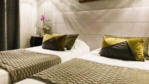 A hotel room with two beds, a nightstand with a lamp and a vase, a framed picture on the wall, and a chandelier. - Brit Hotel Acacias (Arles)