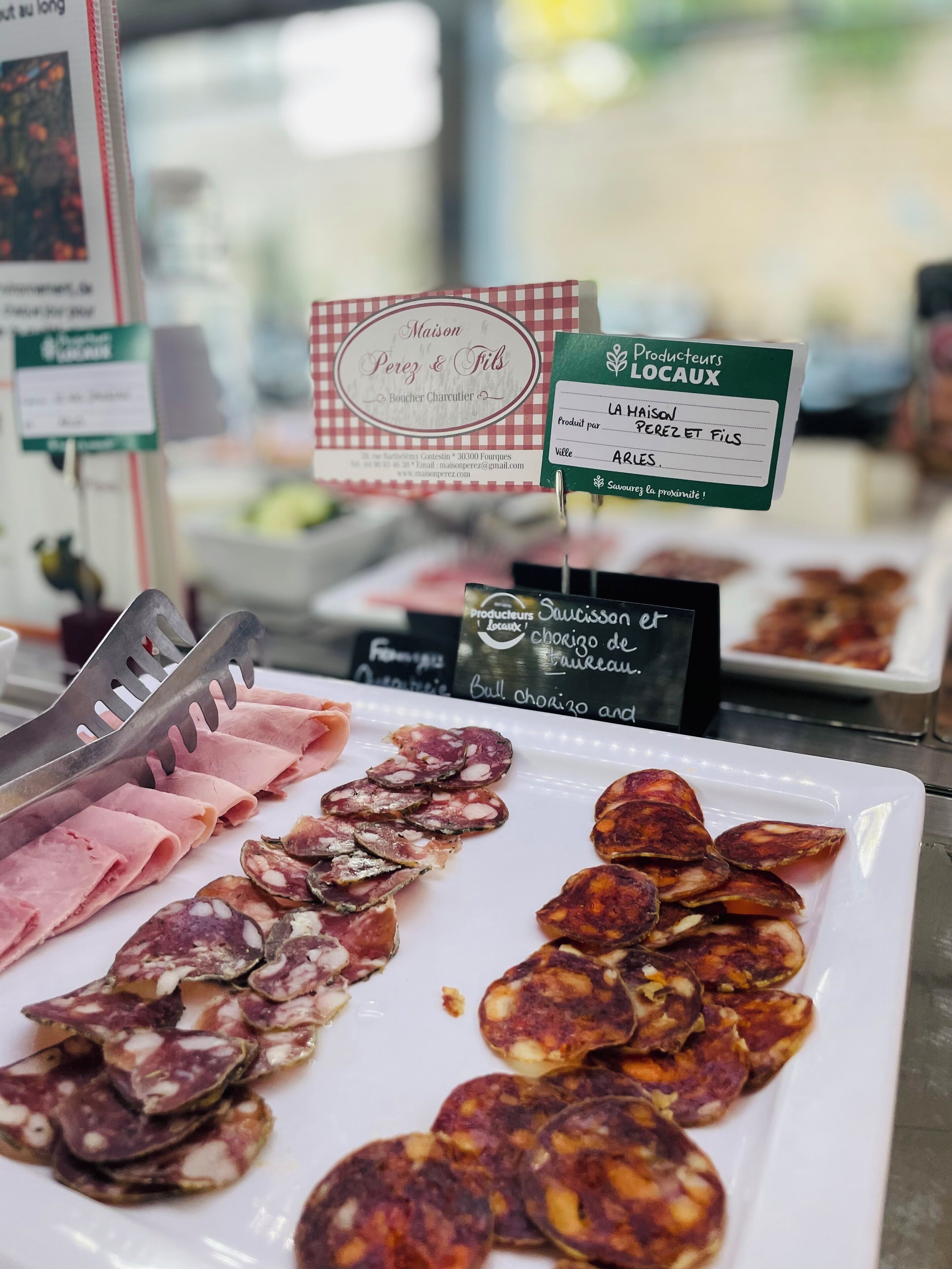Une présentation de différentes sortes de charcuteries sur une assiette blanche, avec des étiquettes indiquant le type et l’origine de chaque produit.