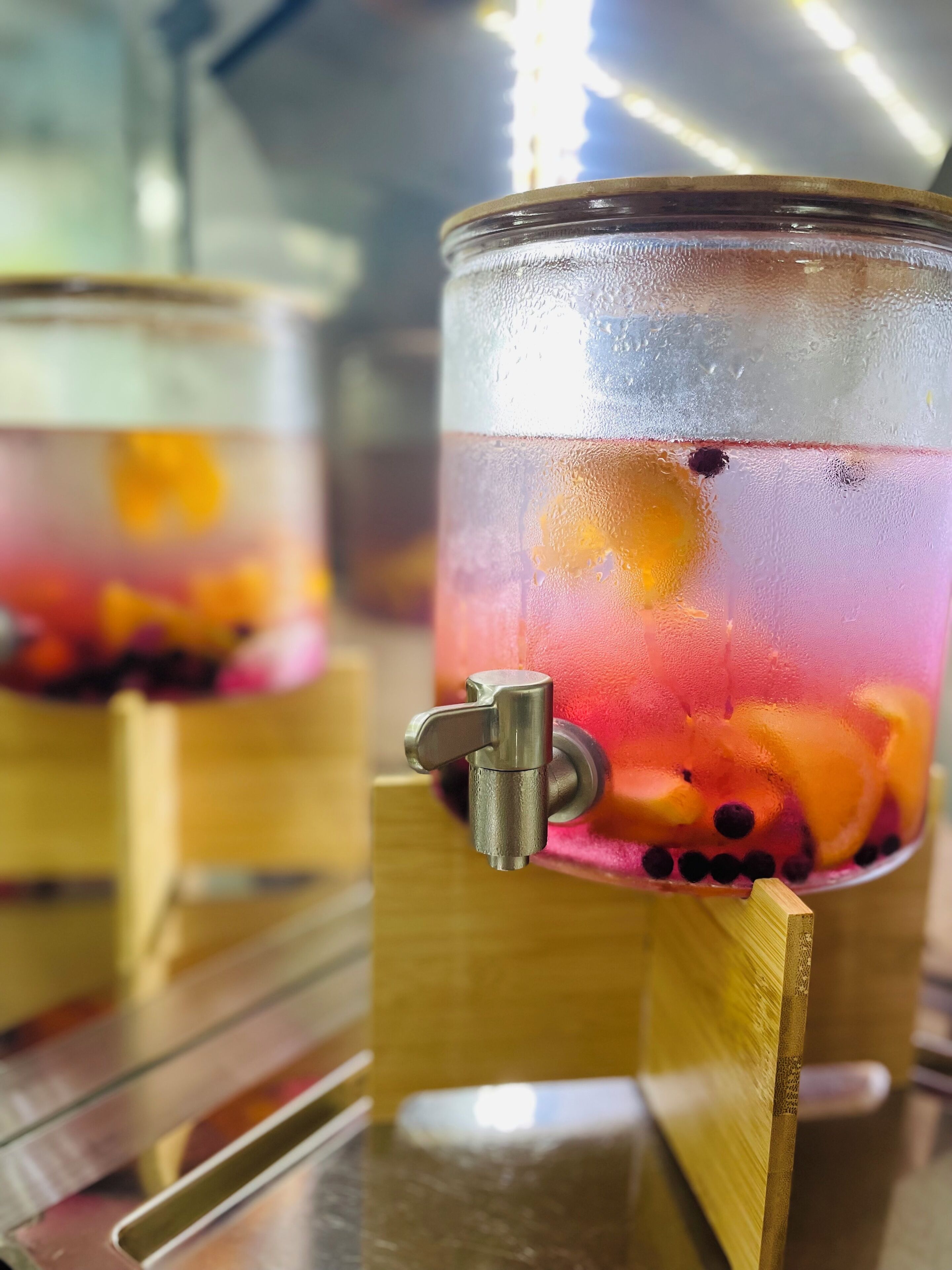 A beverage dispenser with a clear glass container filled with a colorful drink and fruit pieces.