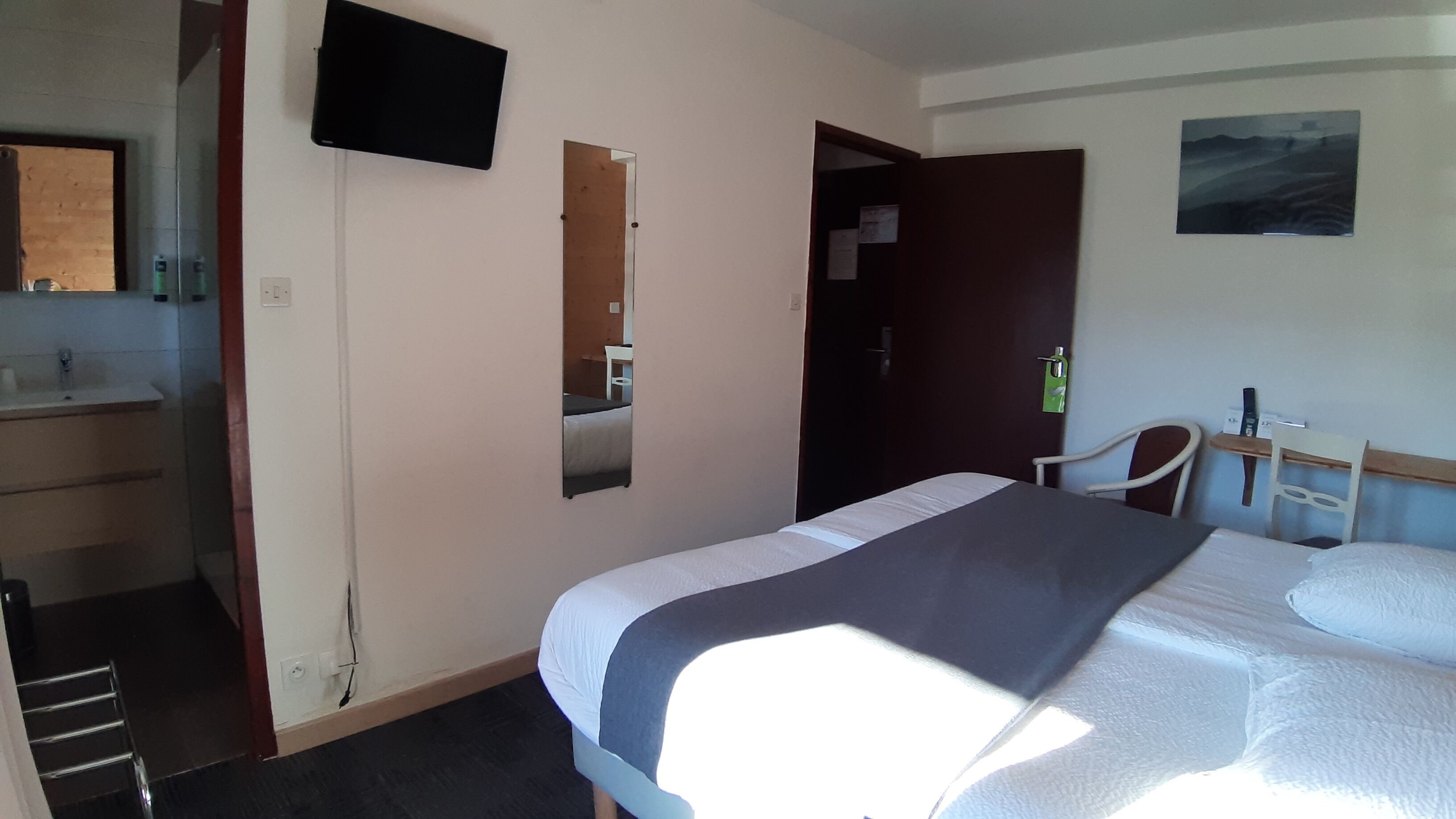 A hotel room with a bed, a desk, a chair, a TV, and a bathroom.