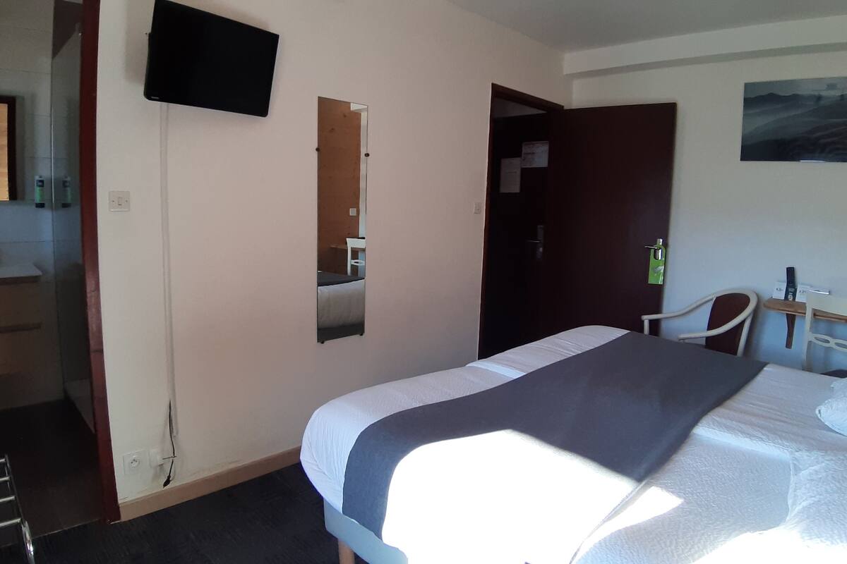 A hotel room with a bed, a desk, a chair, a TV, and a bathroom.