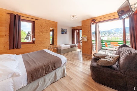 A wooden-paneled room with a bed, a sofa, a TV, and a balcony with a view.