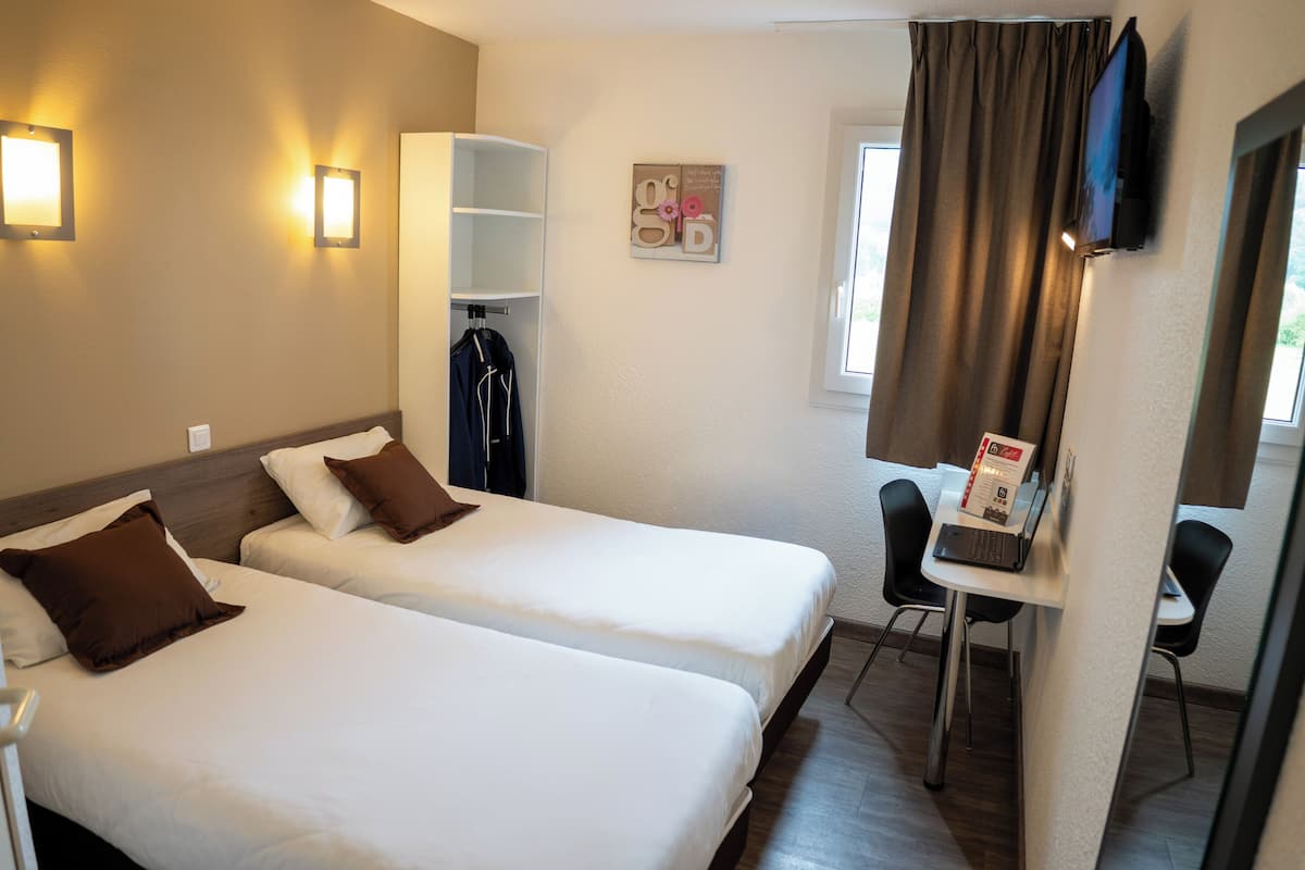 A hotel room with two beds, a desk with a chair, a TV, and a window with curtains.