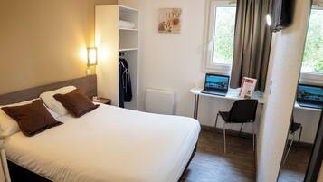 A hotel room with a bed, a desk with a laptop, a chair, and a coat rack.
