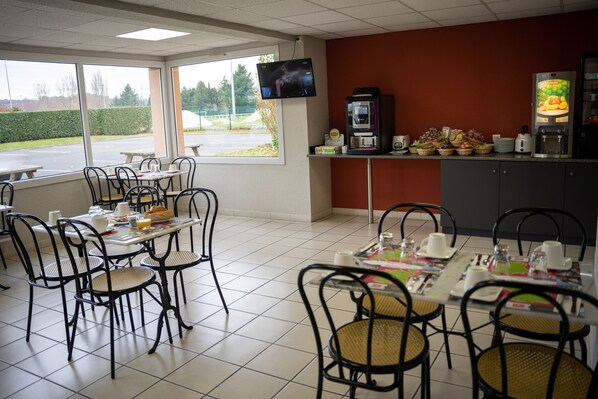A dining area with tables and chairs, a coffee machine, and a television on the wall.