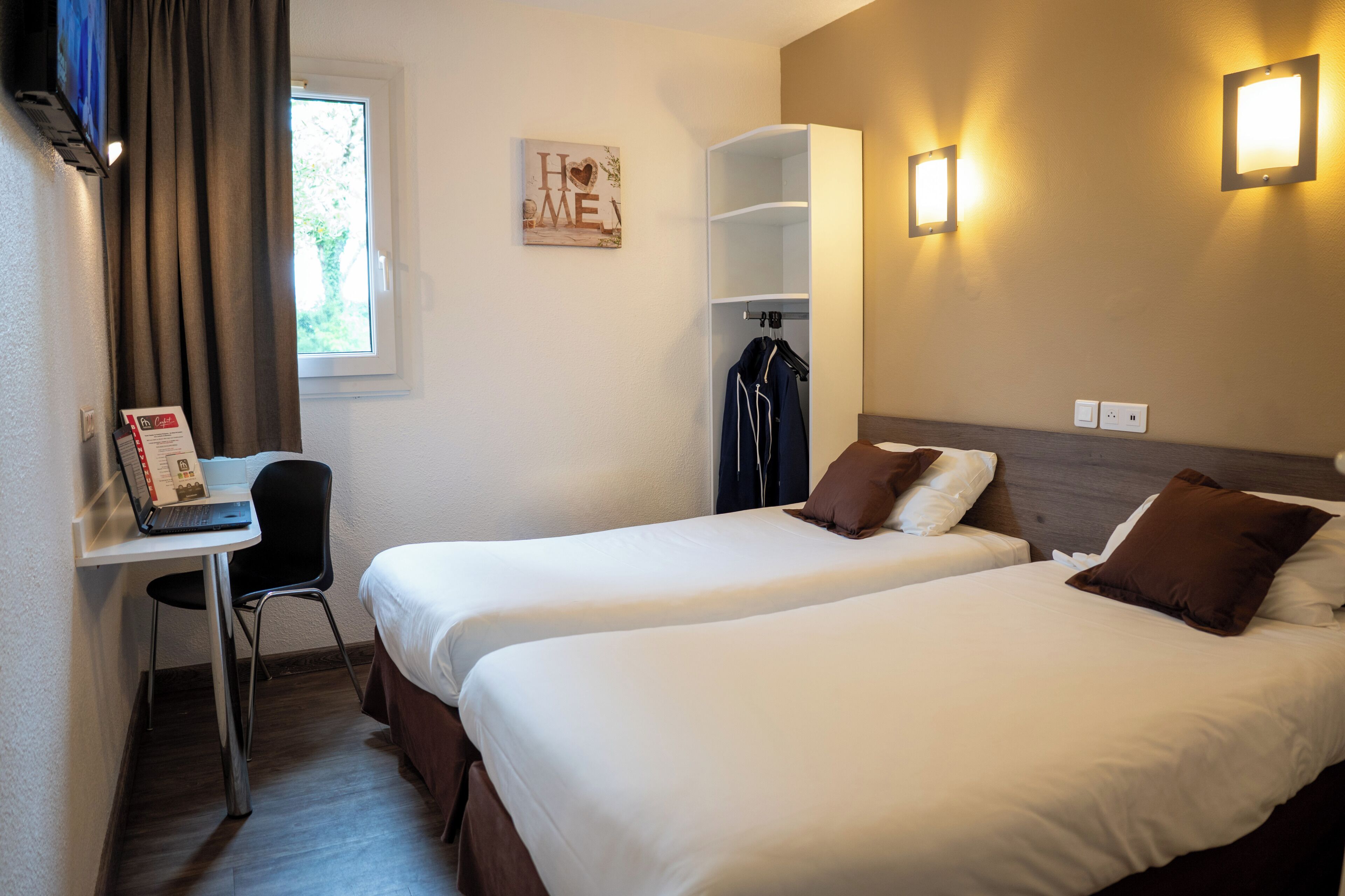 Une chambre d’hôtel avec deux lits, un bureau avec une chaise, un porte-manteau et une fenêtre avec des rideaux.