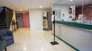 Uma área de recepção de hotel com balcão, frigorífico, máquina de vendas e escadas.
