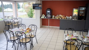 Um restaurante com mesas, cadeiras, uma máquina de café e uma televisão na parede.