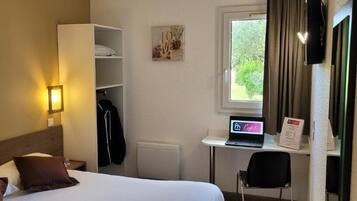 Habitación de hotel con cama, escritorio con computadora portátil, silla, perchero y ventana con cortinas.
