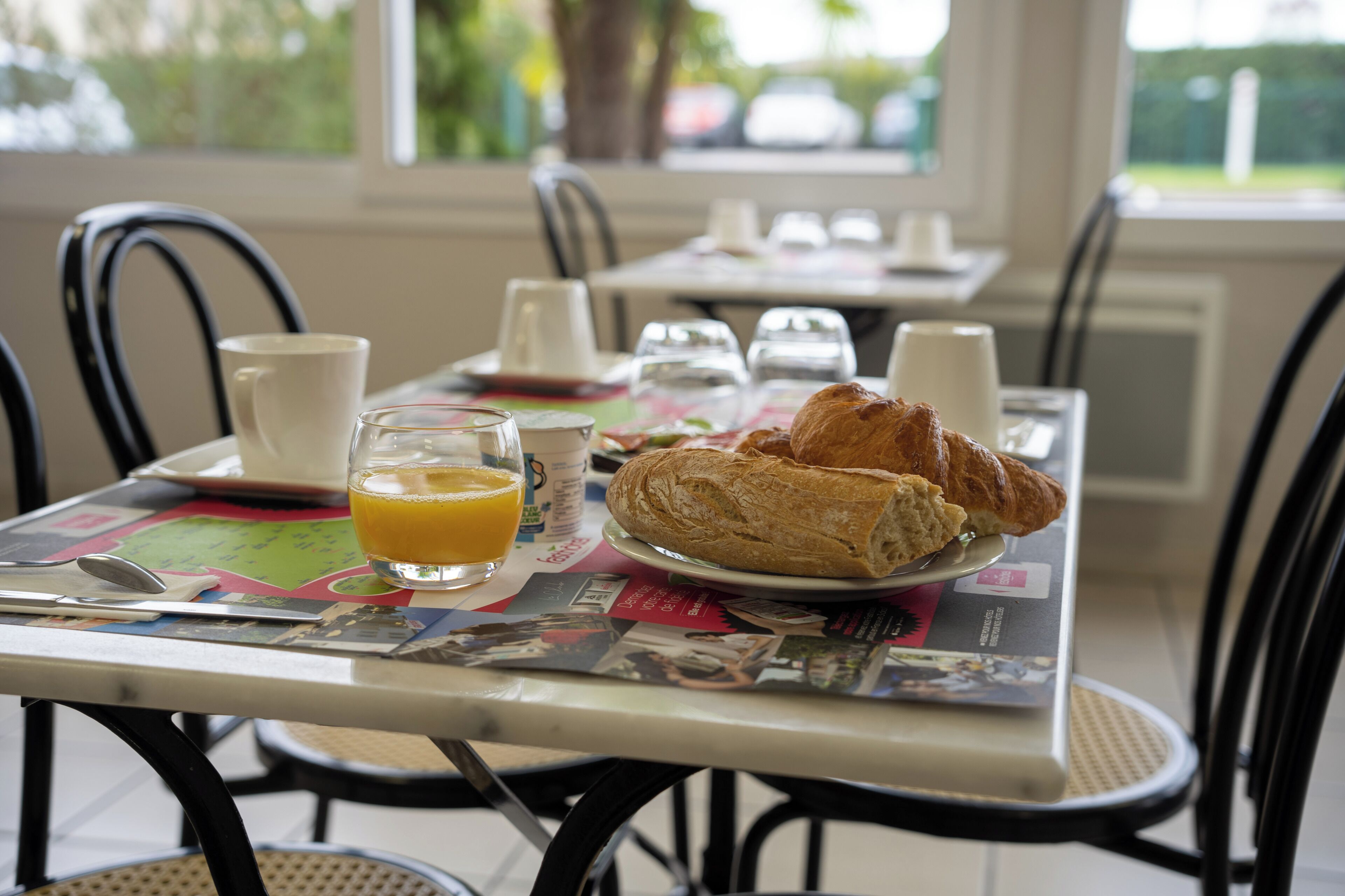A breakfast table with croissants, orange juice, and a newspaper.