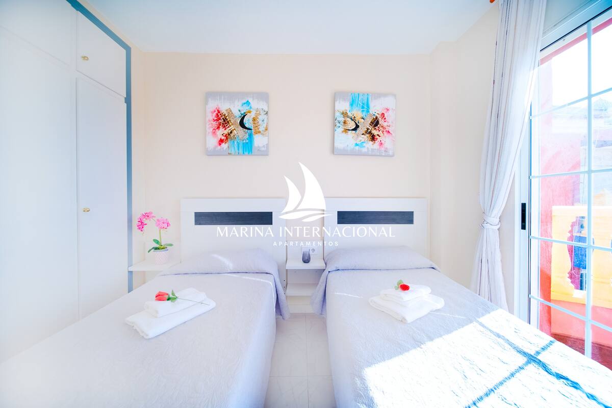 Ein Hotelzimmer mit zwei Betten, einem Nachttisch, einer Vase mit Blumen und einem Bild an der Wand.