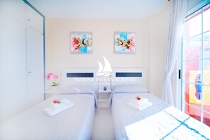 Una habitación de hotel con dos camas, una mesita de noche, un florero con flores y obras de arte en la pared.