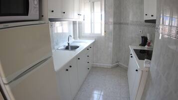 A kitchen with white cabinets, a microwave, a sink, and a window.