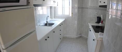 A kitchen with white cabinets, a microwave, a sink, and a window.