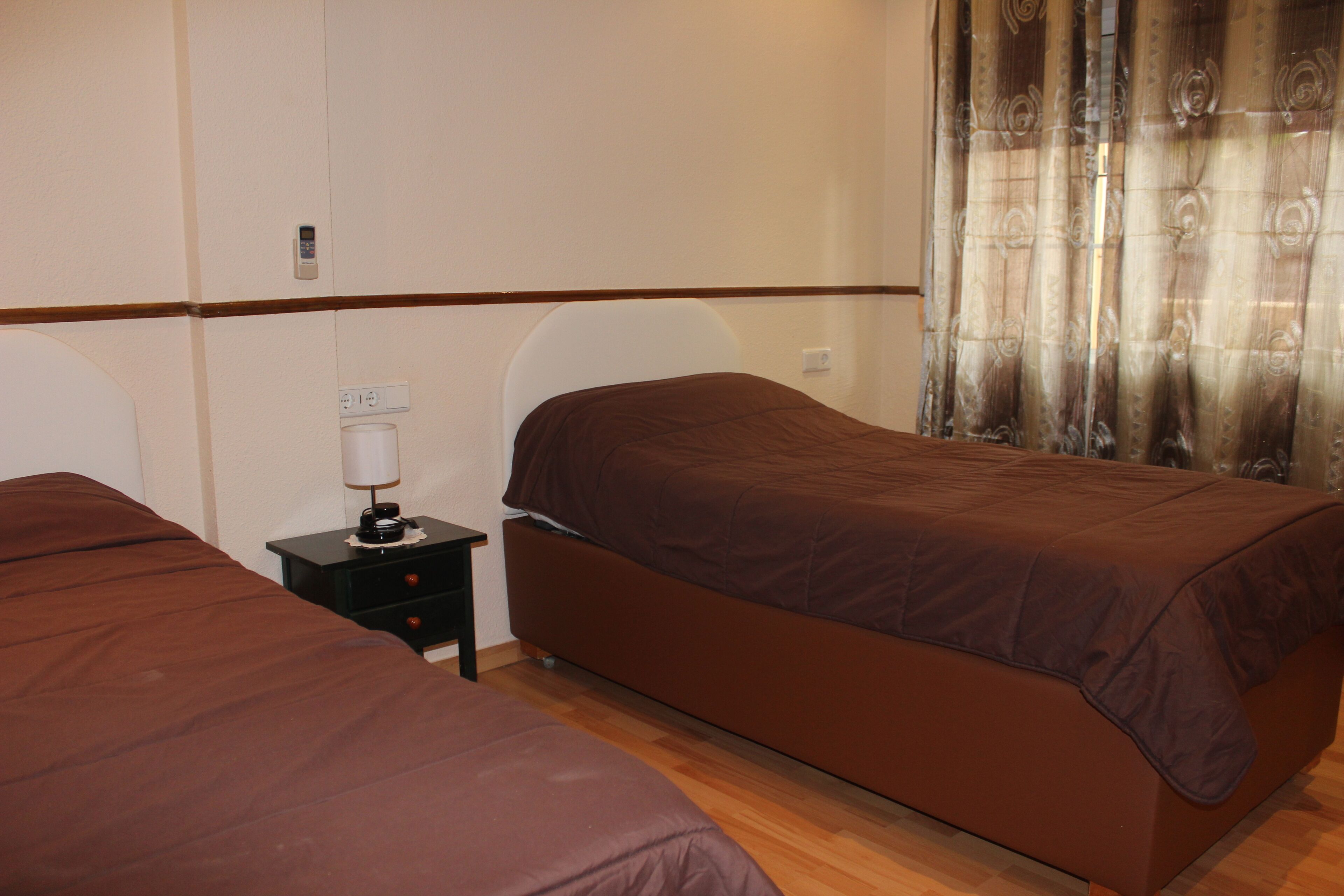 A hotel room with two beds, a nightstand with a lamp, and a curtain.