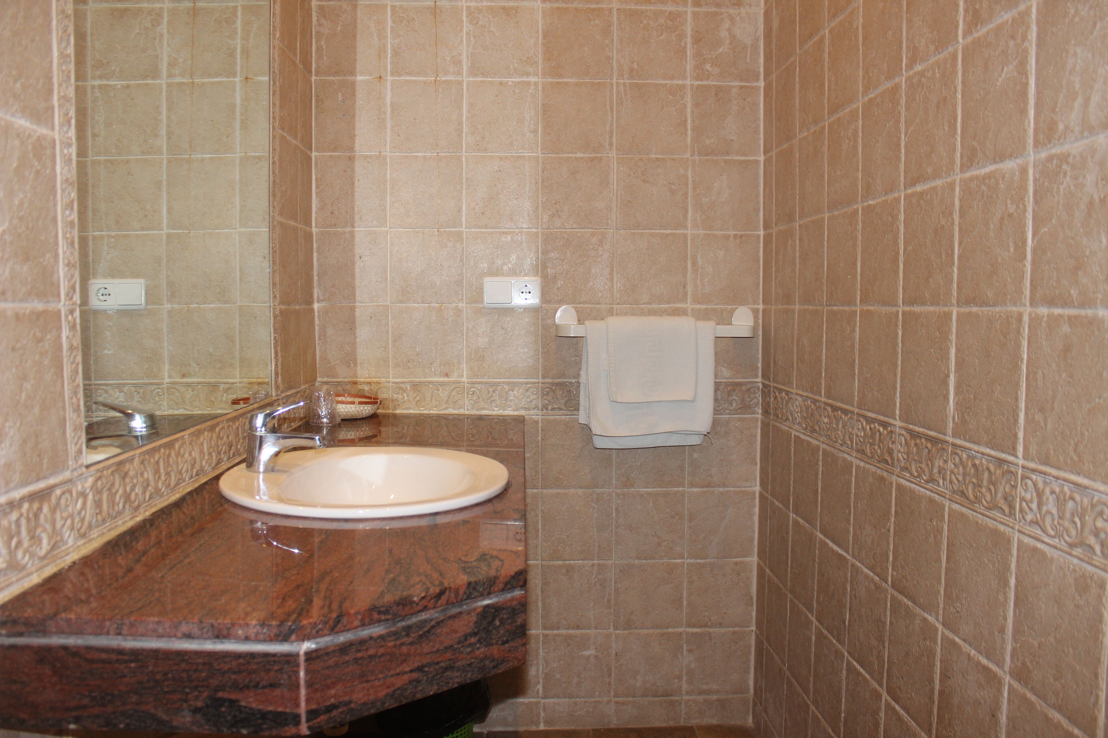 Un baño con lavamanos de mármol, un espejo y un perchero para toallas.