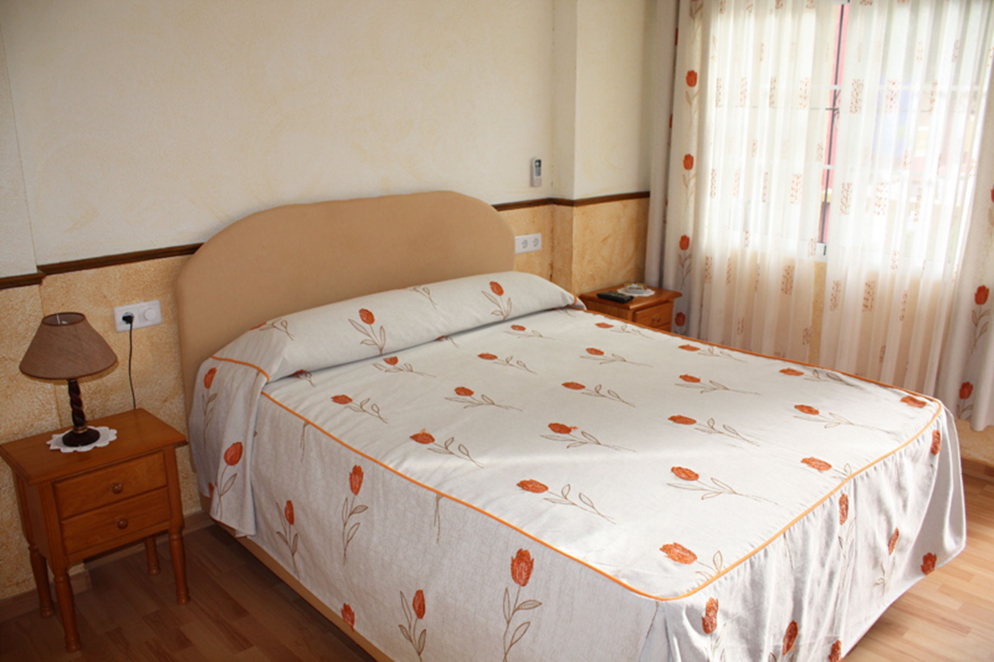 A bedroom with a bed, nightstand, lamp, and curtains.
