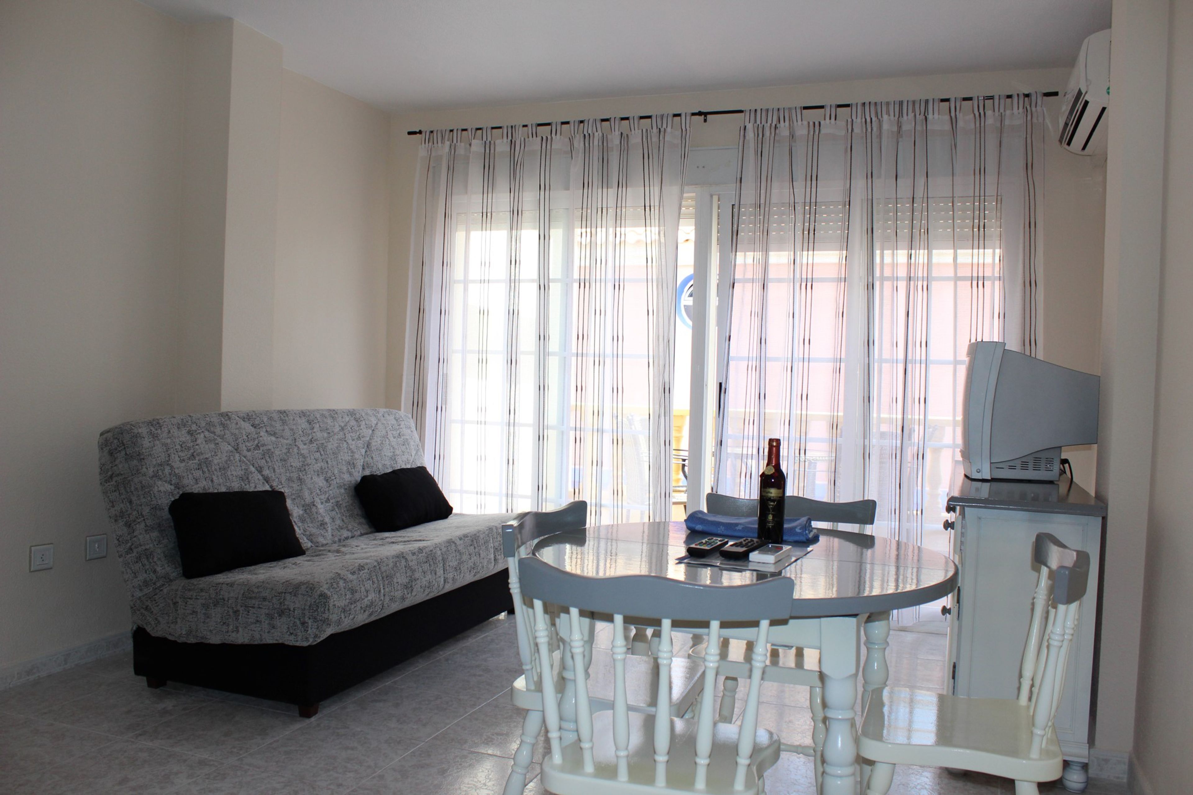 A living room with a sofa, a dining table with chairs, a television, and a window with curtains.