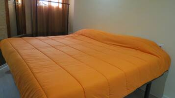 Een bed met een oranje sprei in een kamer met een houten vloer en een raam met gordijnen.