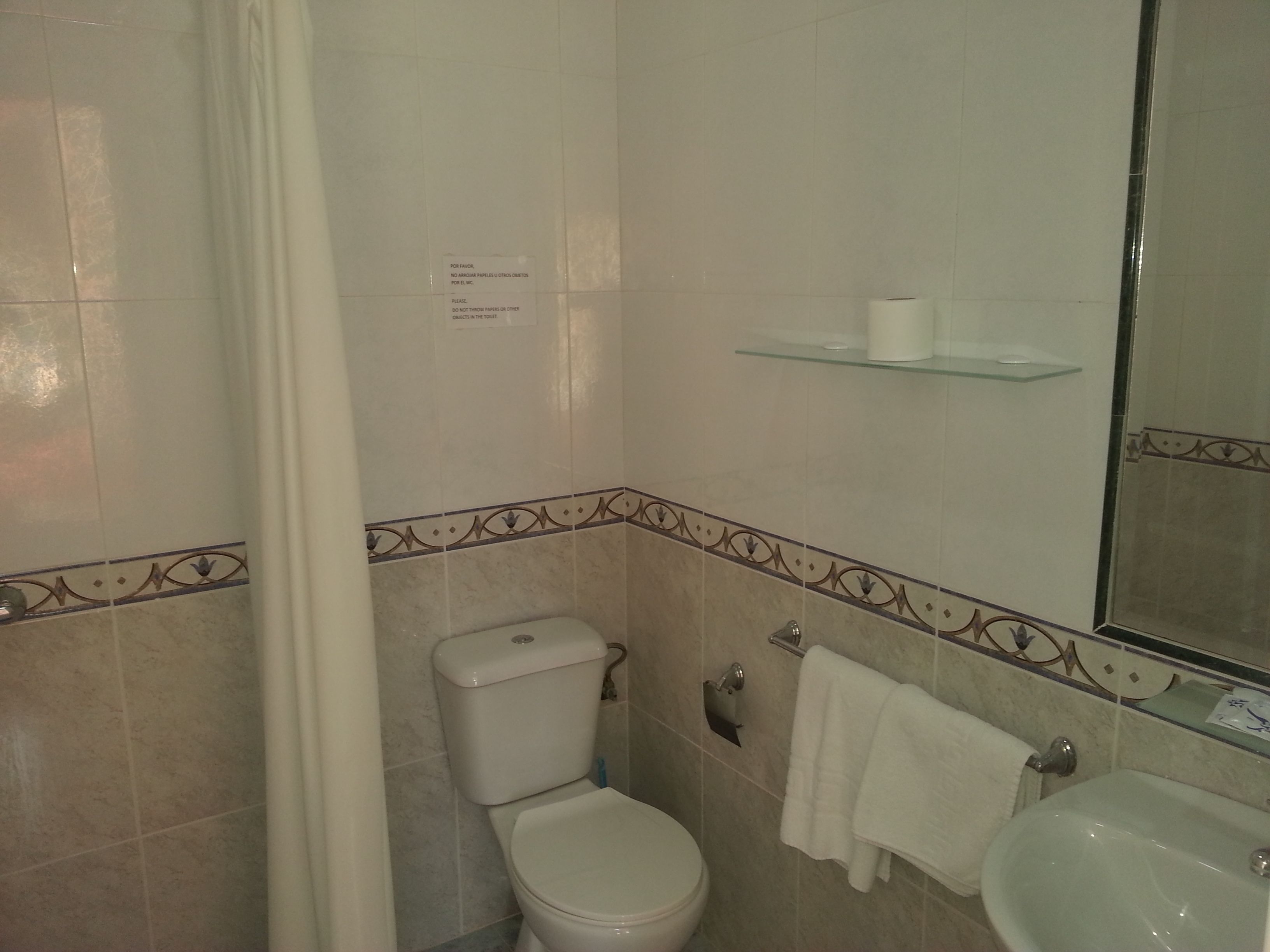 Un baño con inodoro, lavamanos y un estante de vidrio sobre el lavamanos.