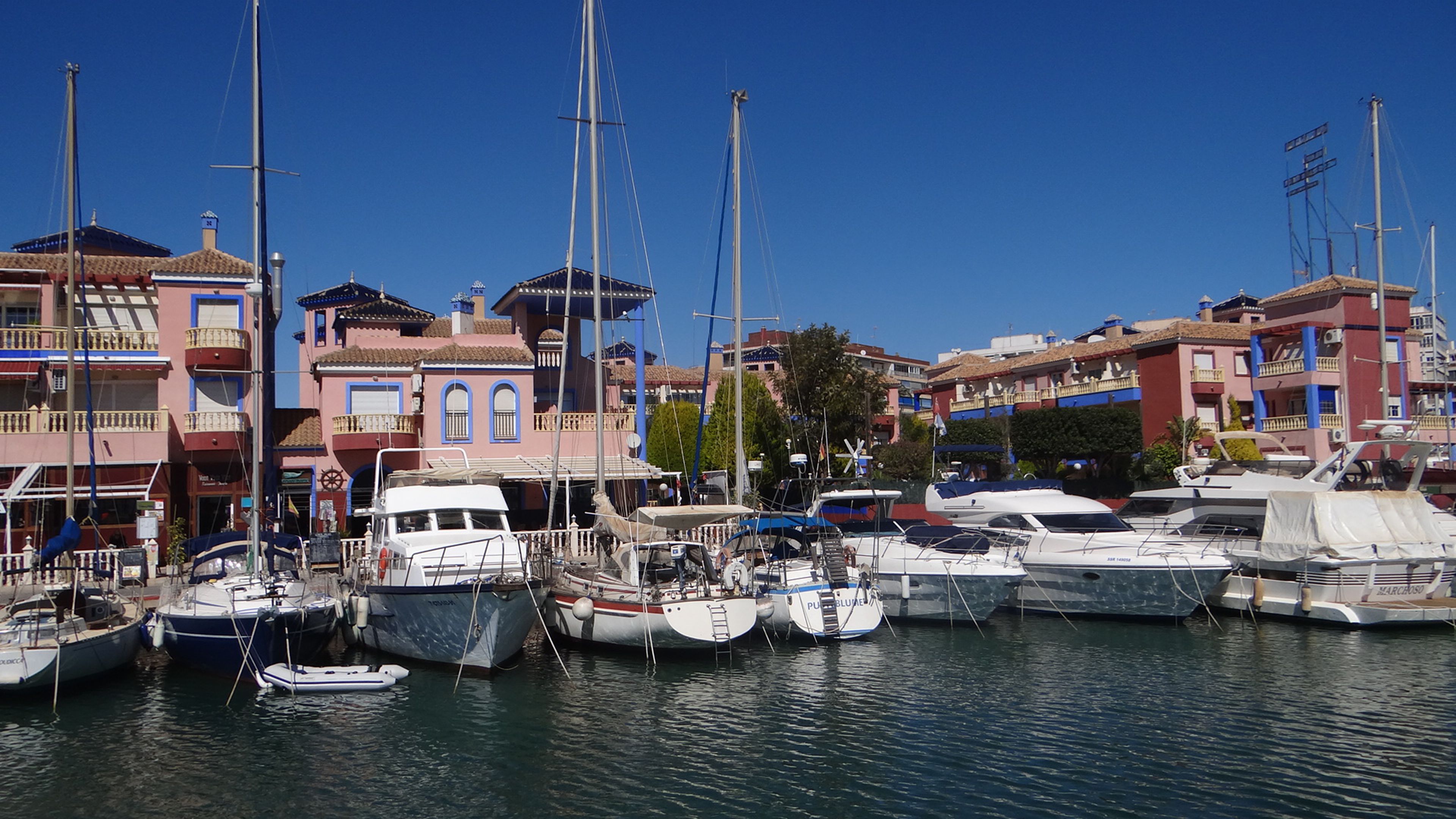 A marina with various boats docked, surrounded by colorful buildings with balconies.