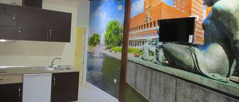 A modern kitchen with a built-in dishwasher, a small dining table, and a mural depicting a cityscape with a statue.