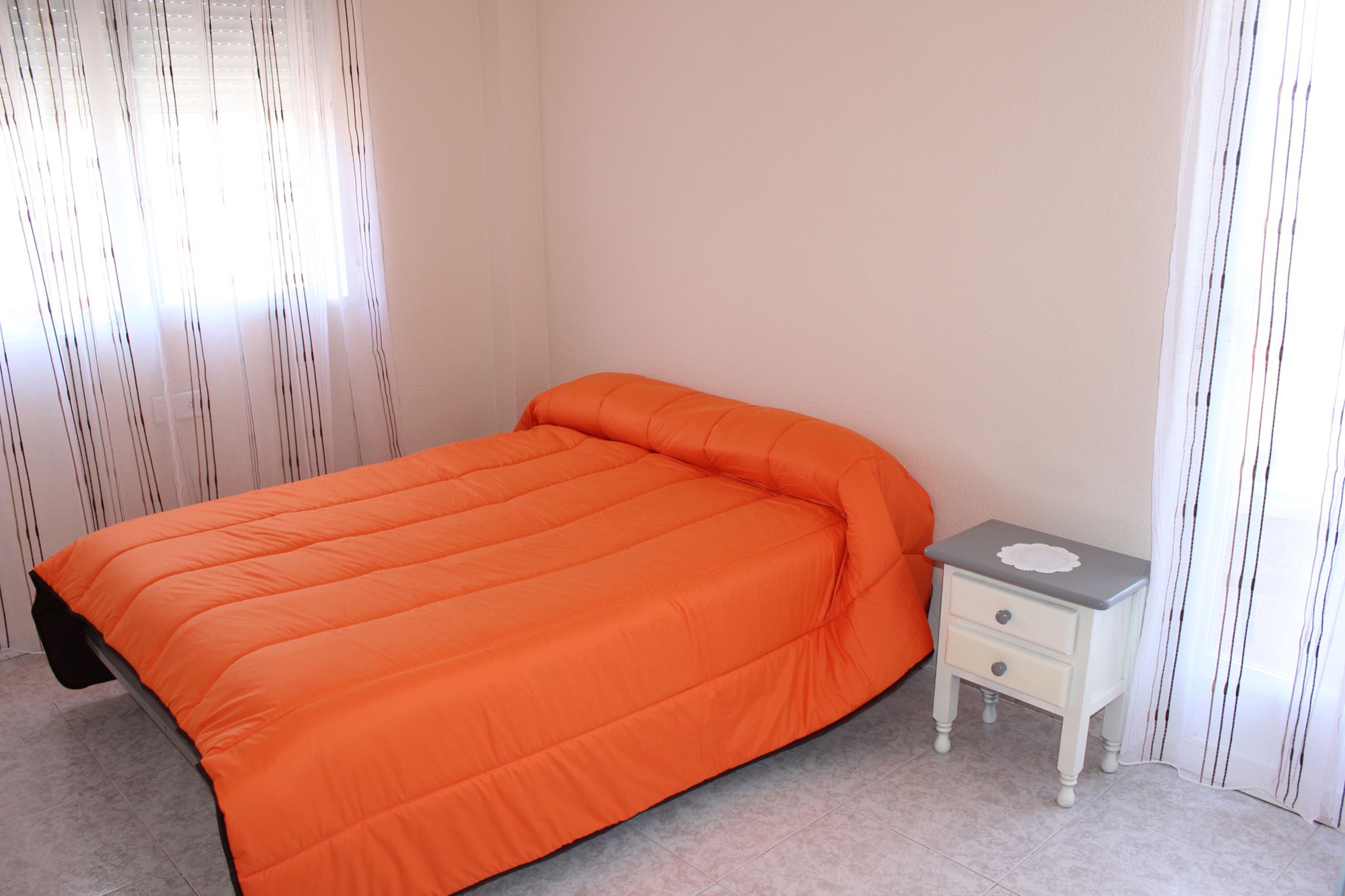 Un dormitorio con una cama individual, una mesita de noche y un ventanal con cortinas.