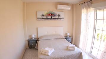 A bedroom with a large bed, a nightstand, a wall-mounted air conditioner, and a window with curtains.