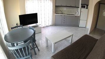 A compact living space with a dining area, a television, a kitchenette, and a door.