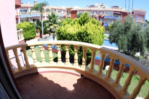 Un balcón con barandilla curva, suelo de baldosas y vista a una zona residencial con edificios de varios pisos y vegetación.