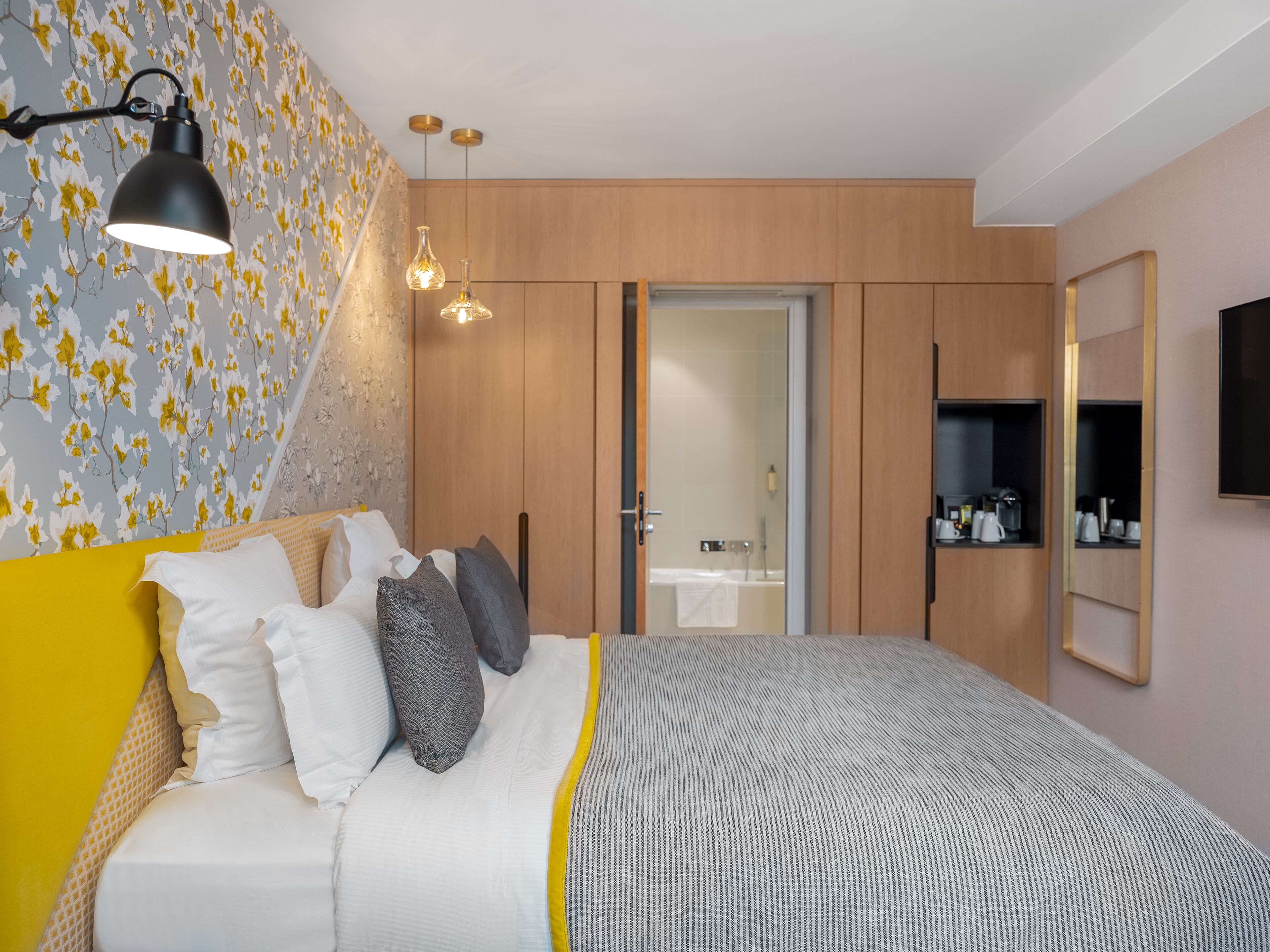 Un dormitorio moderno con una cama, lámparas de noche, un armario y un baño visible a través de una puerta abierta.