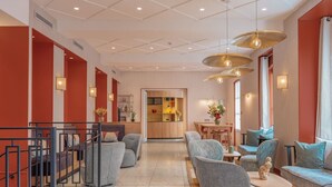En modern hotellobby med en central sittgrupp, en trappa och ett kök som syns genom en öppen dörr.