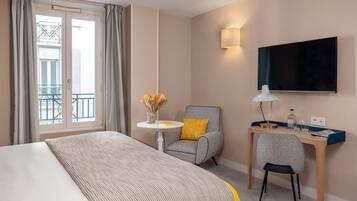 Una habitación de hotel con cama, escritorio, silla, televisión y ventana con cortinas.