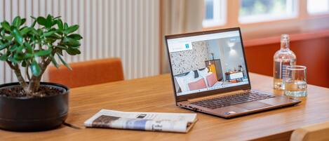 A laptop on a wooden table with a potted plant, a newspaper, and two glasses of water.