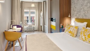 Ett hotellrum med en säng, ett skrivbord, en stol, ett fönster med gardiner och utsikt över omgivningen.