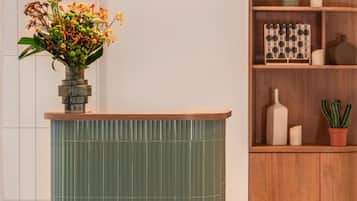 Un pilar verde con textura vertical y un estante superior de madera que sostiene un florero con flores.